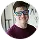 Portrait of a young person wearing glasses and a maroon shirt, smiling against a white background.